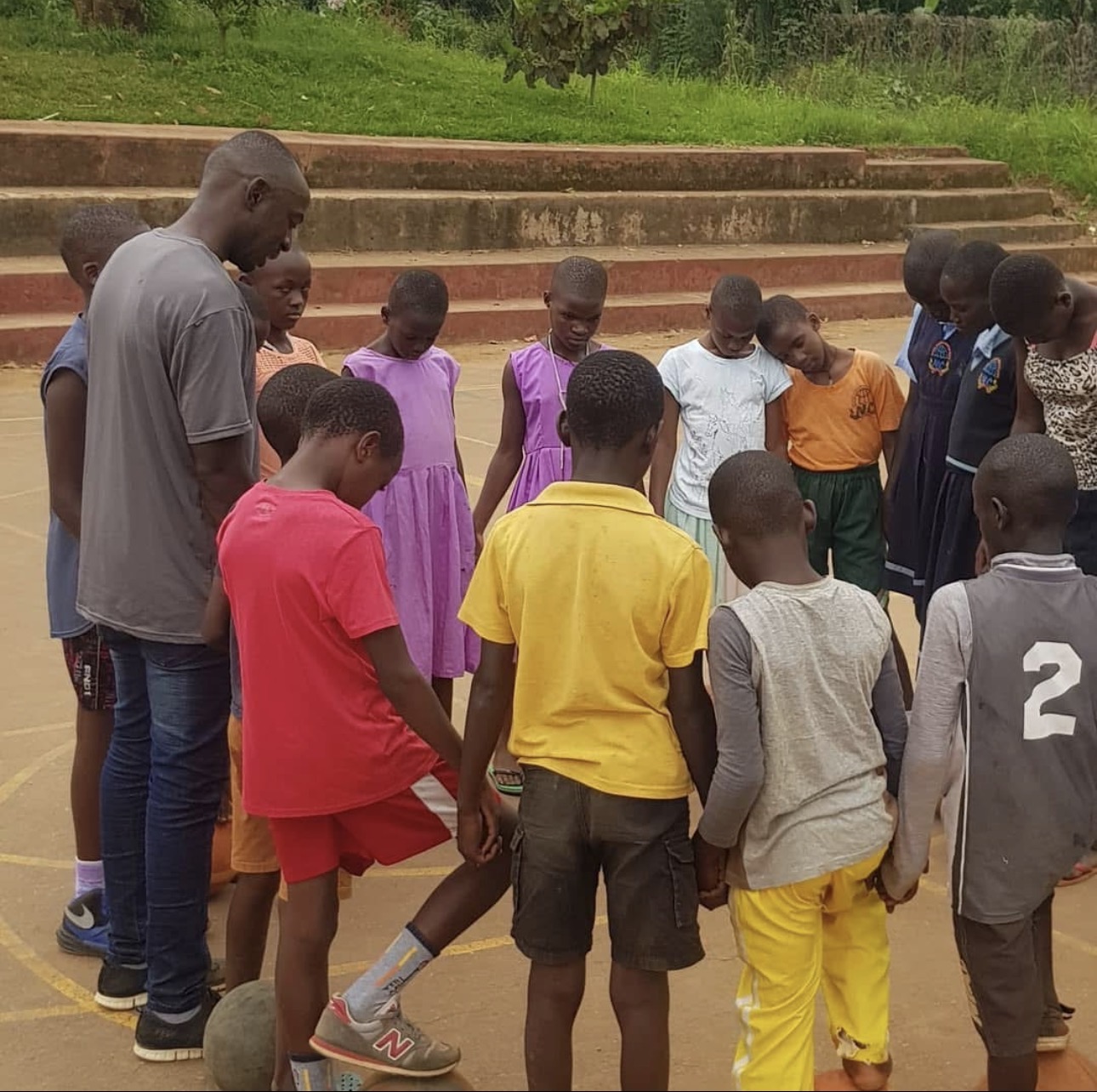 Coach and children standing in a prayer circle on the court