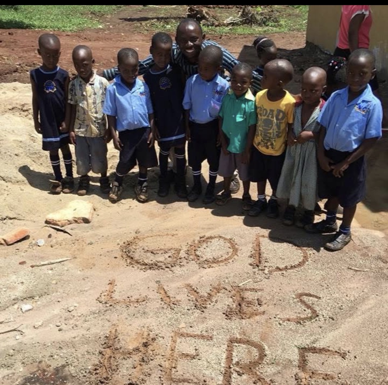 Young students beside 'God Lives Here' written in the sand